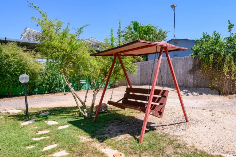 נדנדת עץ אדומה בחצר המוריקה של הבית
